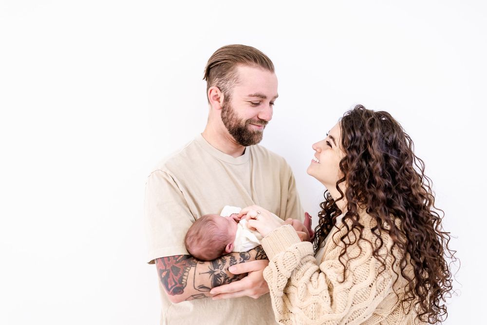 A couple in neutral sweaters share a tender moment while standing against a white background.