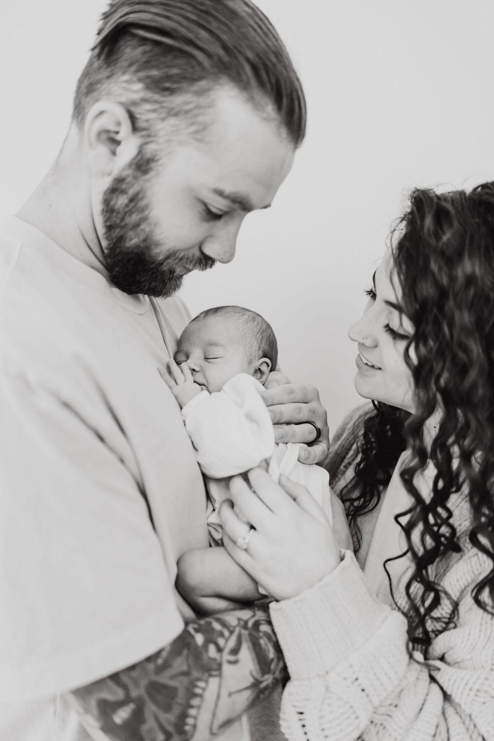 Black and white portrait of parents with a newborn baby in tender embrace wearing light colored knit sweaters.
