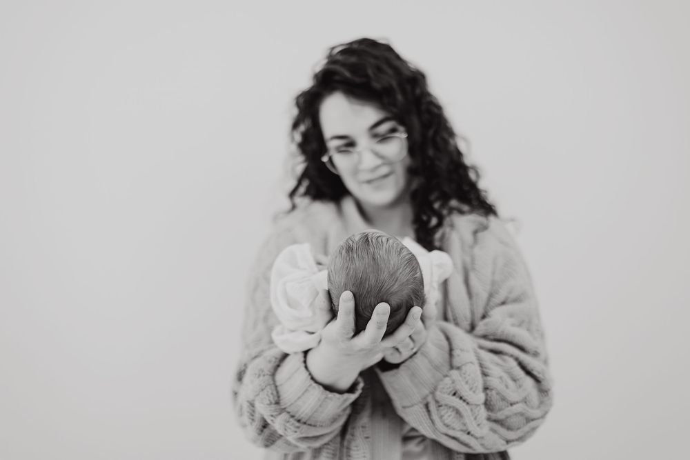 Person in a cozy sweater smiles while gently holding and admiring a natural coconut against a white backdrop.