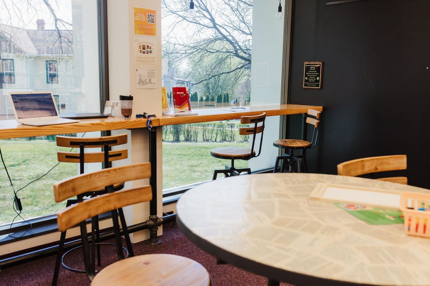 Modern cafe-like interior with wooden bar seating along windows, round marble table and minimalist decor overlooking green lawn.