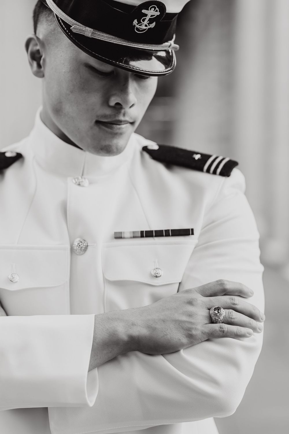 Naval officer in white dress uniform adjusting cuff detail in black and white portrait.