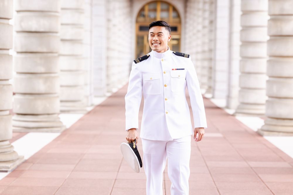 Military officer in white dress uniform standing confidently in front of classical architecture.