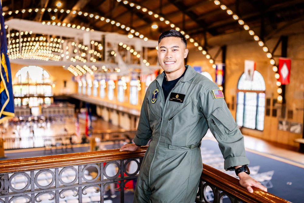 Service member in flight suit poses in vintage military museum with string lights overhead.