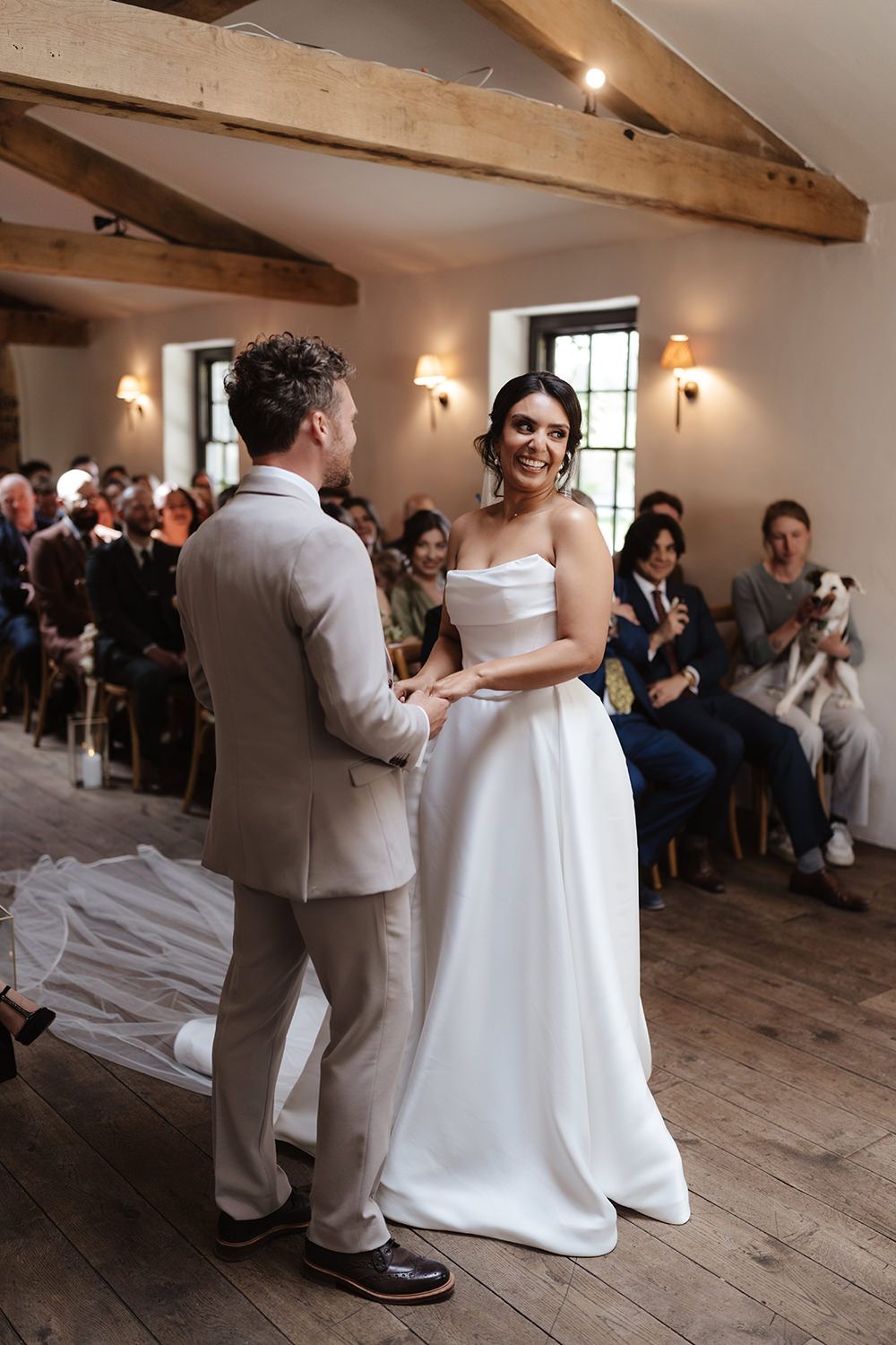 A couple shares a joyful moment during their wedding ceremony in a rustic venue with exposed wooden beams.