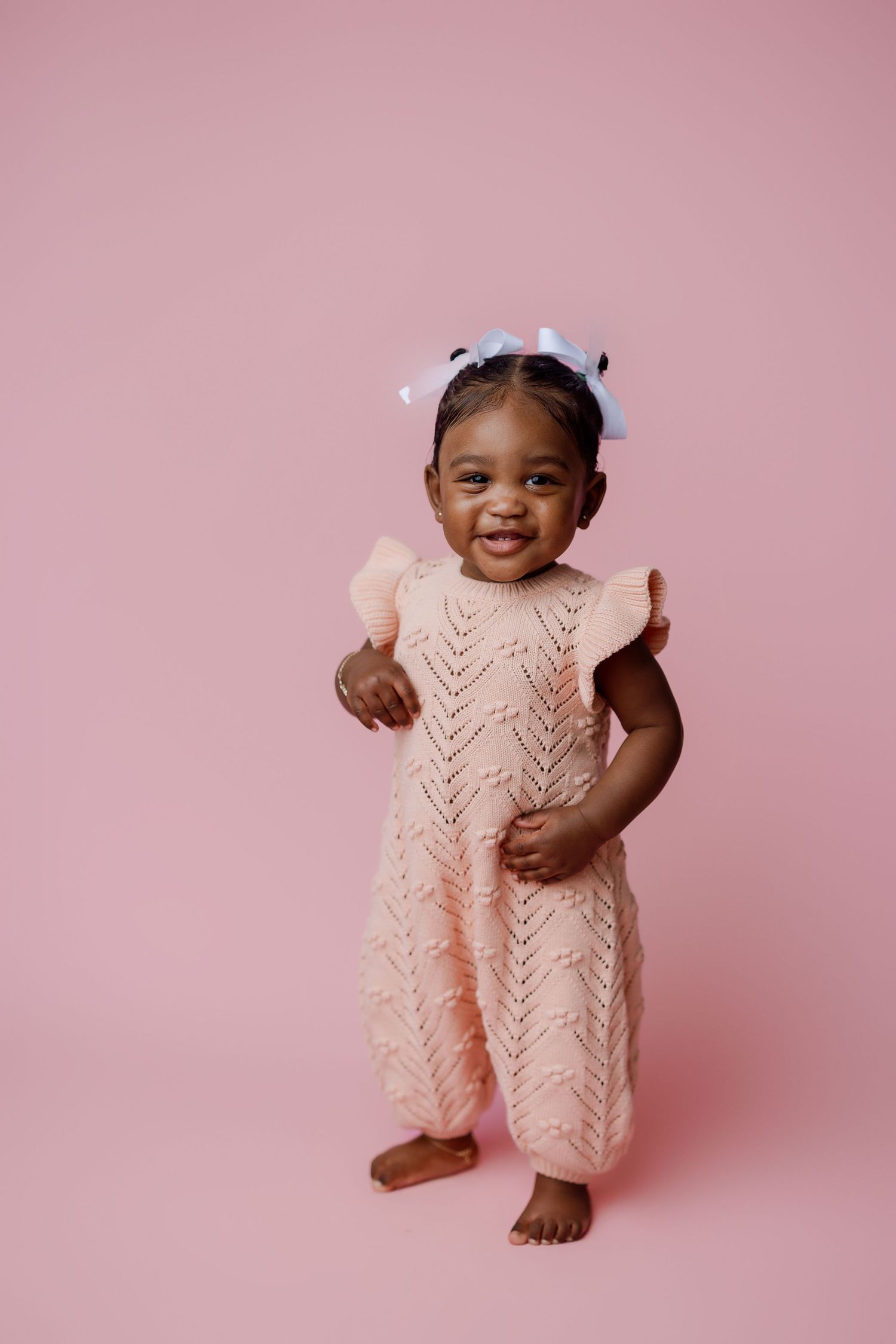Baby in pink knit romper poses against pink backdrop with adorable expressions in photo series.