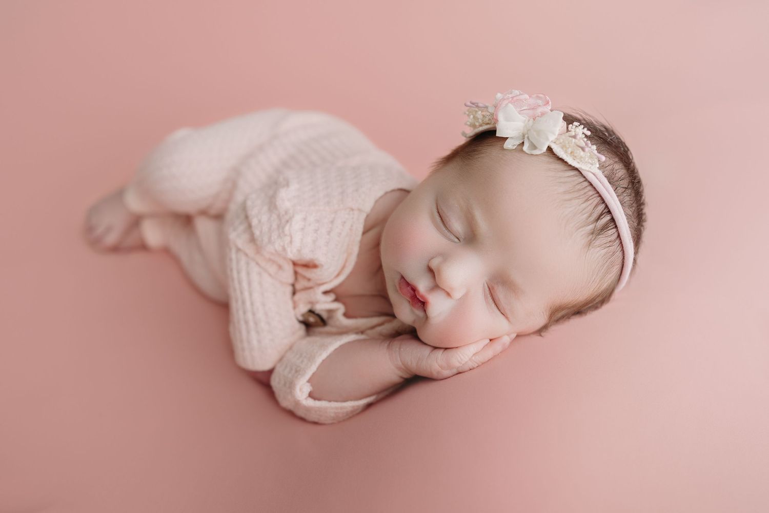 A baby in a pink tulle dress celebrates their first birthday with balloon decorations in soft pink, white and rose gold.
