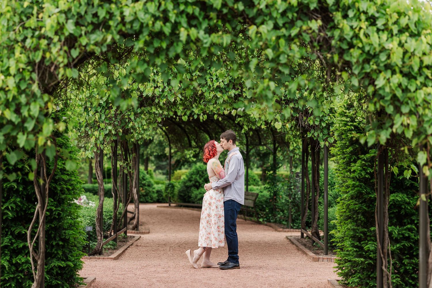 A couple embraces in a romantic garden walkway surrounded by lush green vine-covered archways. Cantigny Park