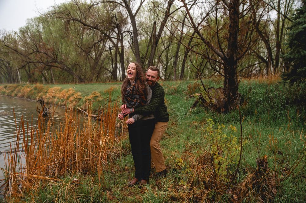 A person stands by a peaceful pond surrounded by autumn reeds and bare trees in a natural setting.