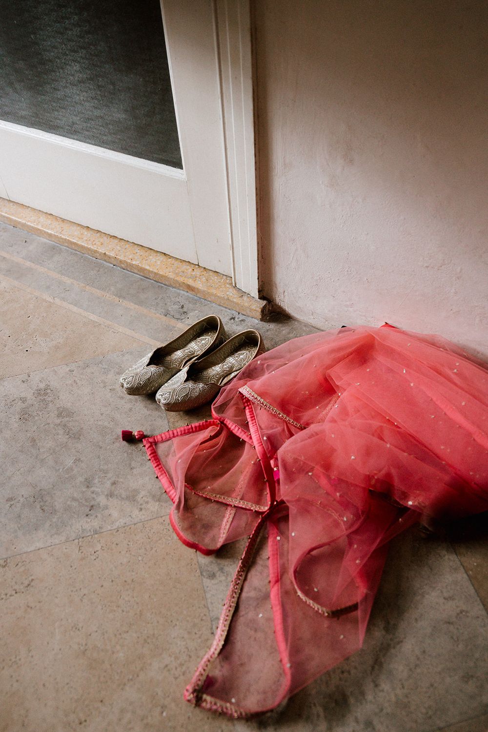 A red tulle dress and ballet shoes lay on a concrete floor beside a white wall.
