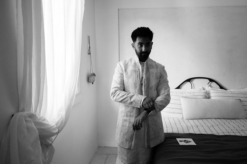 A figure in a white shirt stands in a bright minimalist bedroom interior with natural light filtering through curtains.