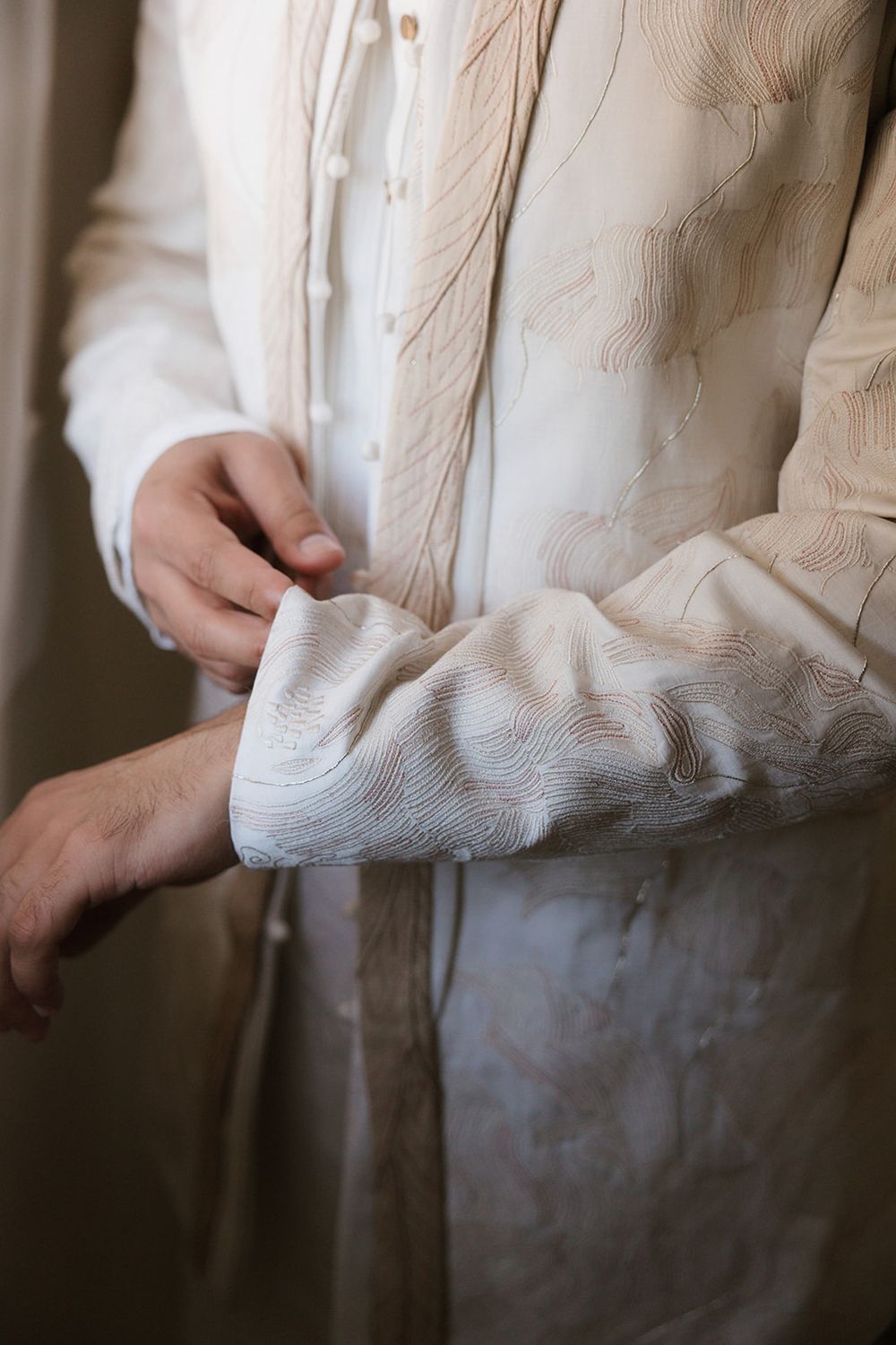 Close-up view of hands adjusting the sleeve of an elegant white textured dress shirt.