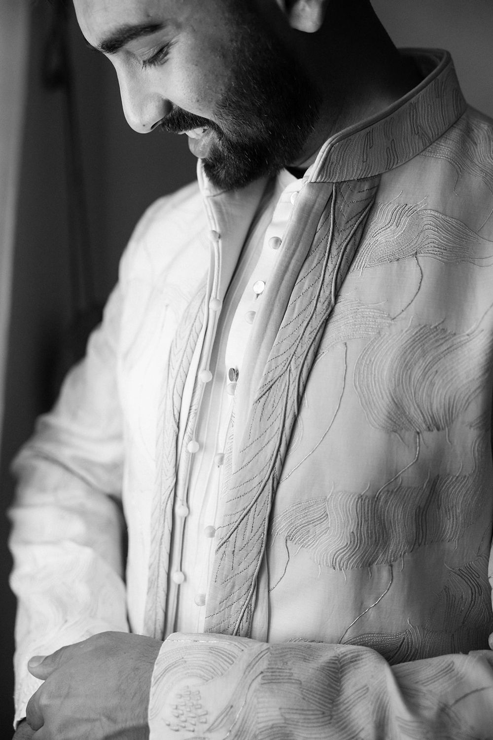Black and white close-up photo showing person wearing an ornately embroidered white dress shirt with textural details.