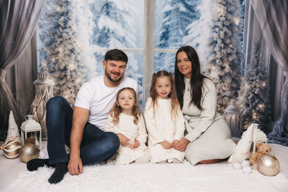 Seasonal winter holiday portrait with snowy backdrop featuring a group sitting together among white decorations and lanterns.