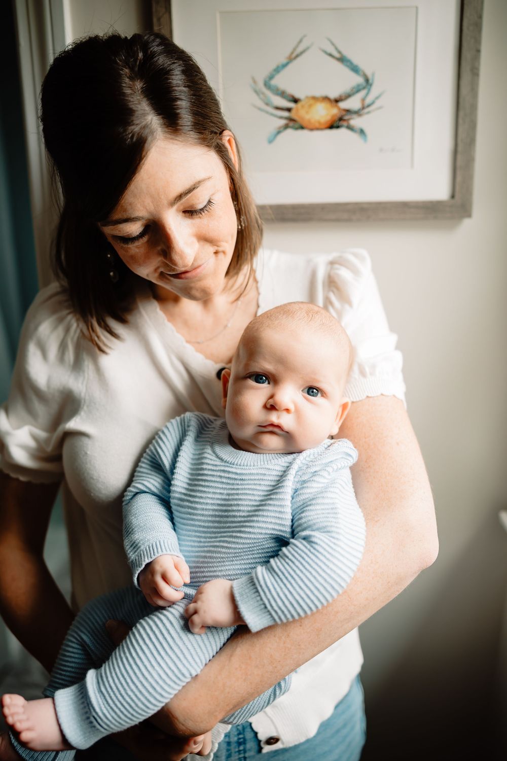 A tender moment between parent and baby in front of a blue crab art print on a wall.