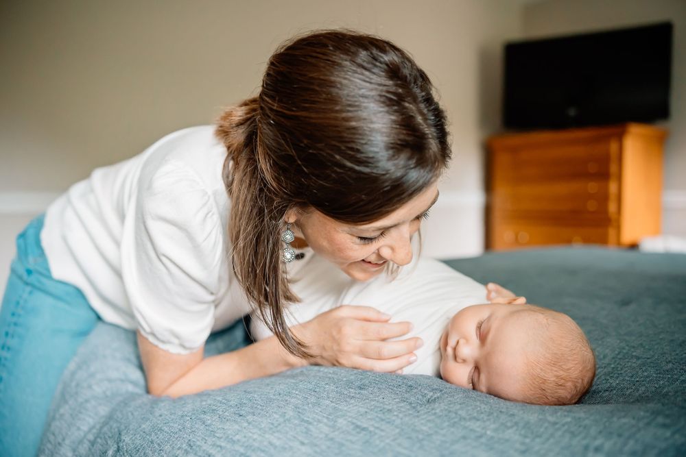 A loving caregiver tenderly interacts with an infant while lying together on a gray bed.
