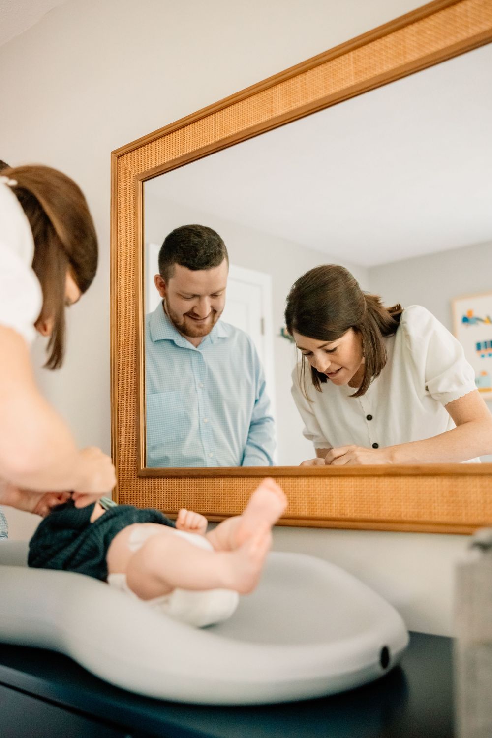 Couple looking down at a baby on a changing table while smiling and interacting with their child in front of a mirror.