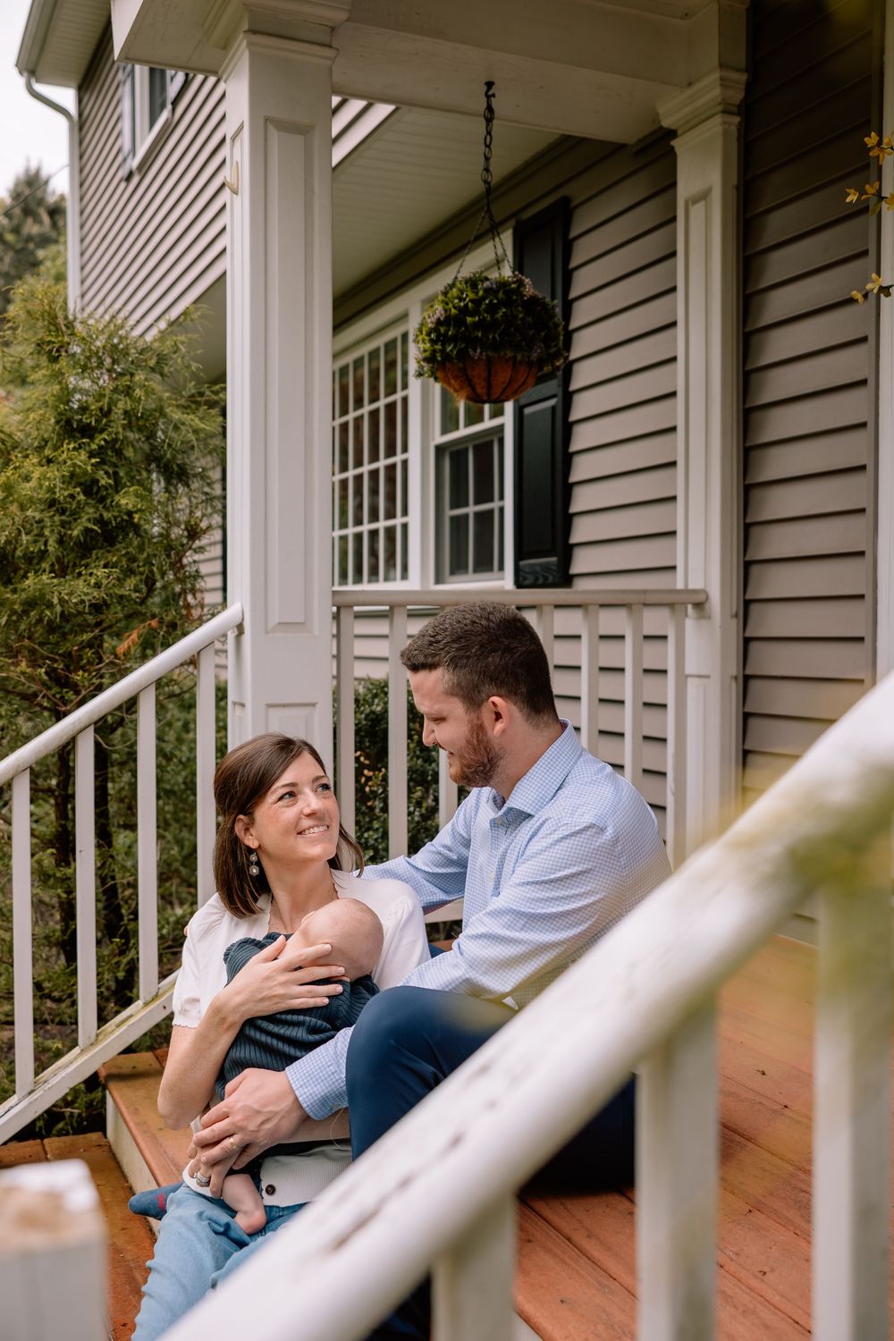 A couple sitting on their front porch steps with their newborn baby.
