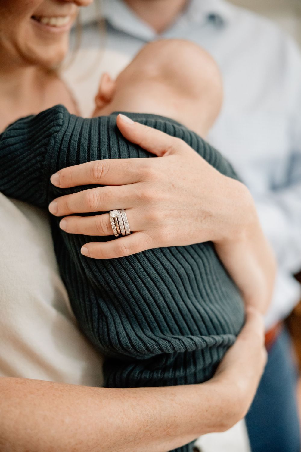 Close up of hands holding a swaddled newborn baby in a dark knit blanket.