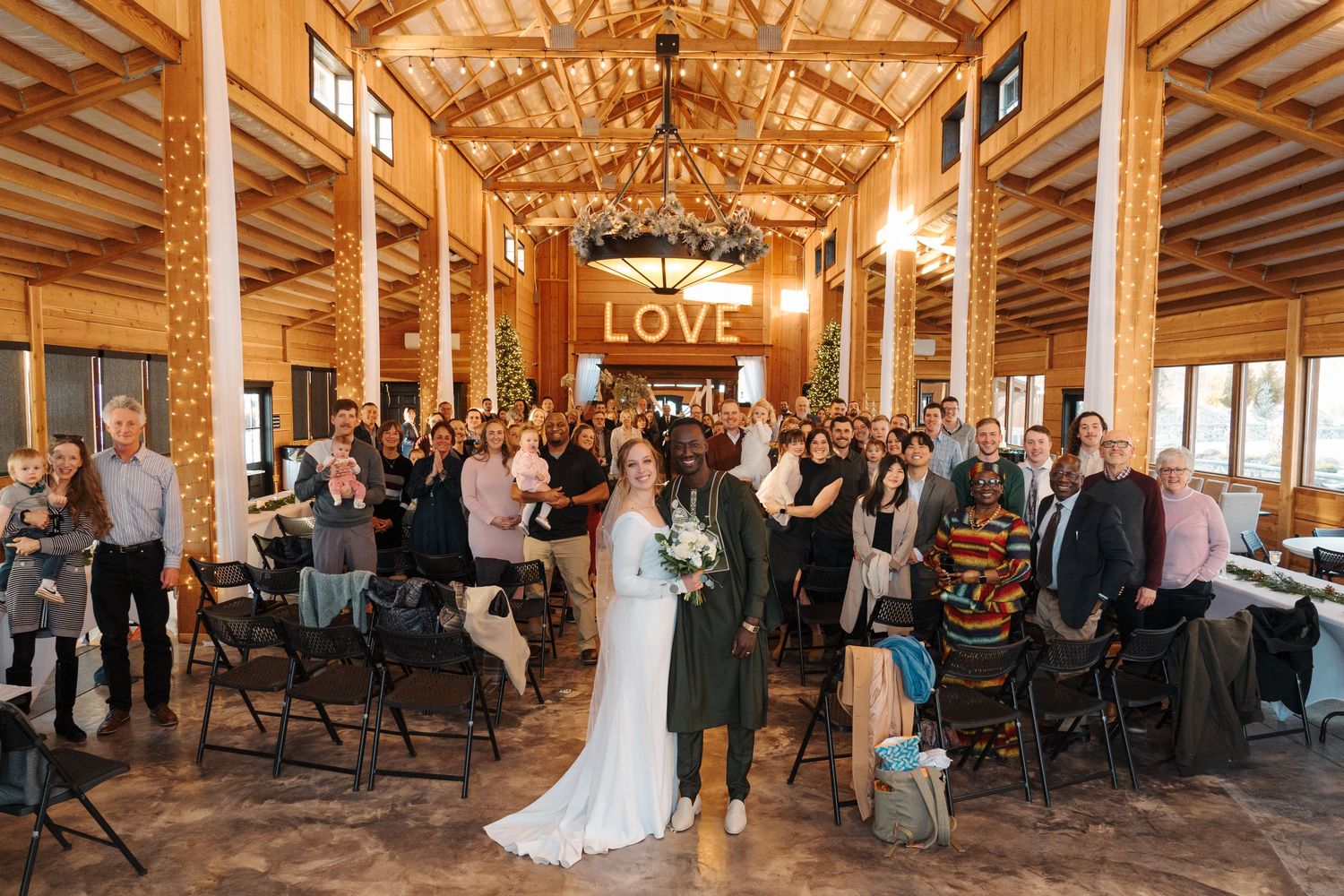 A rustic wooden barn venue with vaulted ceilings hosts an indoor wedding reception with a glowing LOVE sign.