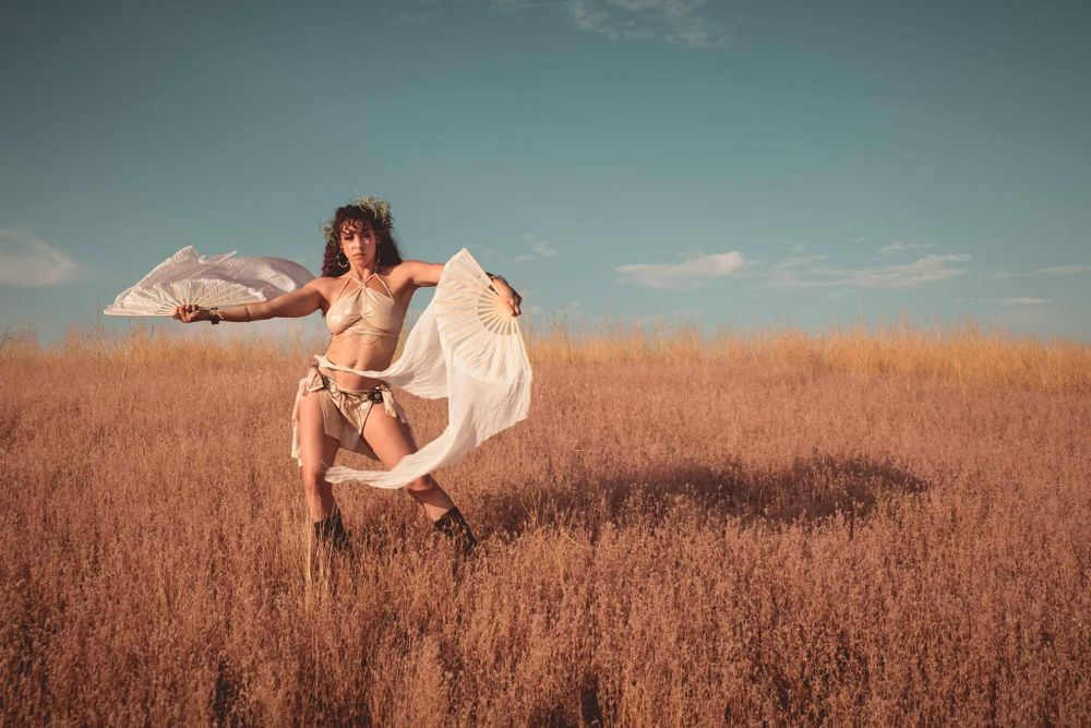Dancer leaps with flowing fabric in sunlit wheat field.