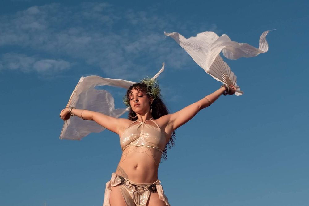 Figure dancing joyfully against blue sky with flowing white fabric in a bikini on a sunny day.