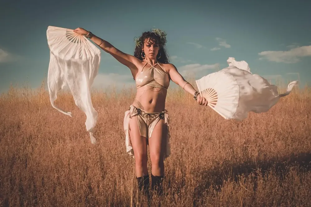 Woman in flowing white fabric poses dramatically in golden wheat field.