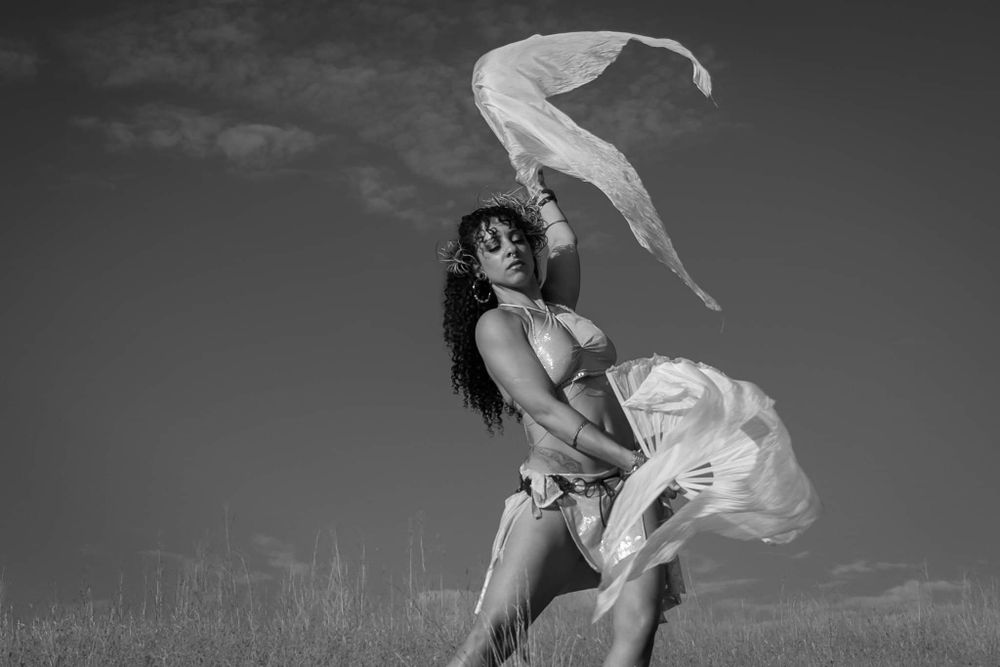 Artistic black and white portrait of dancer with flowing fabric in field.