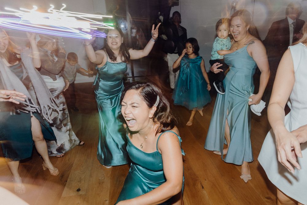 Wedding party guests in teal bridesmaid dresses dancing energetically captured by Apertured Media Auckland Wedding Photographer.