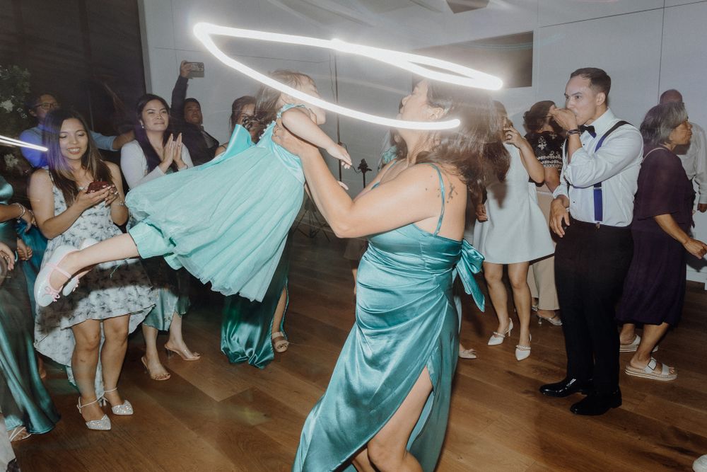 A group of wedding party guests dance energetically in turquoise dresses captured by Apertured Media Auckland Wedding Photographer.