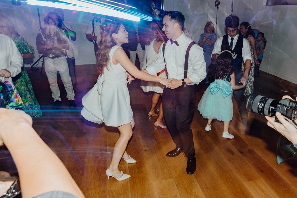 Dancers in light-colored formal attire move energetically captured by Apertured Media Auckland Wedding Photographer.