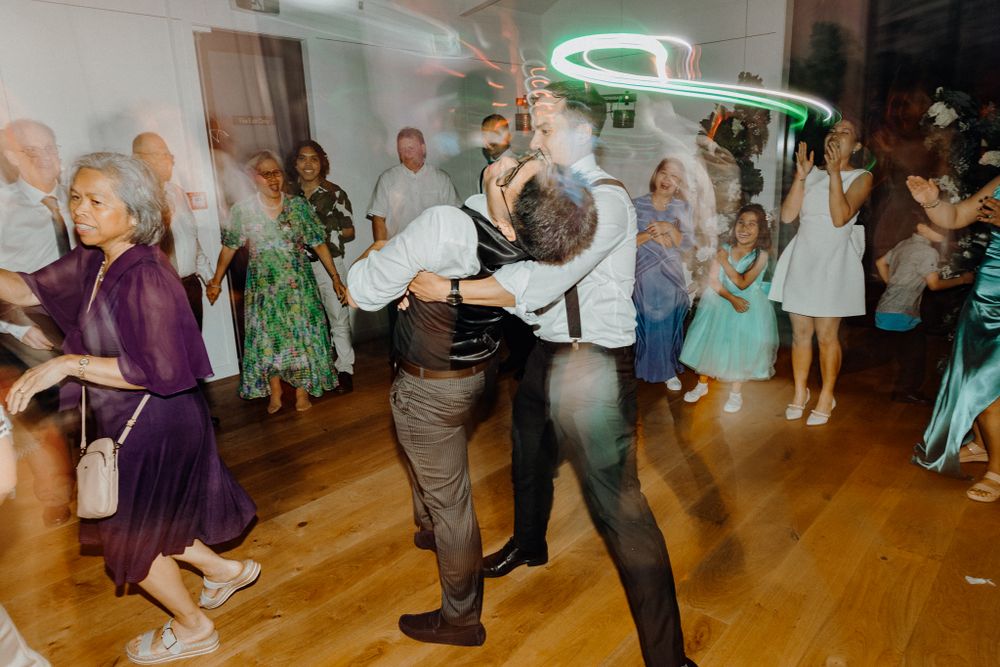 Wedding guests dance and celebrate on a wooden dance floor under neon lighting captured by Apertured Media Auckland Wedding Photographer.