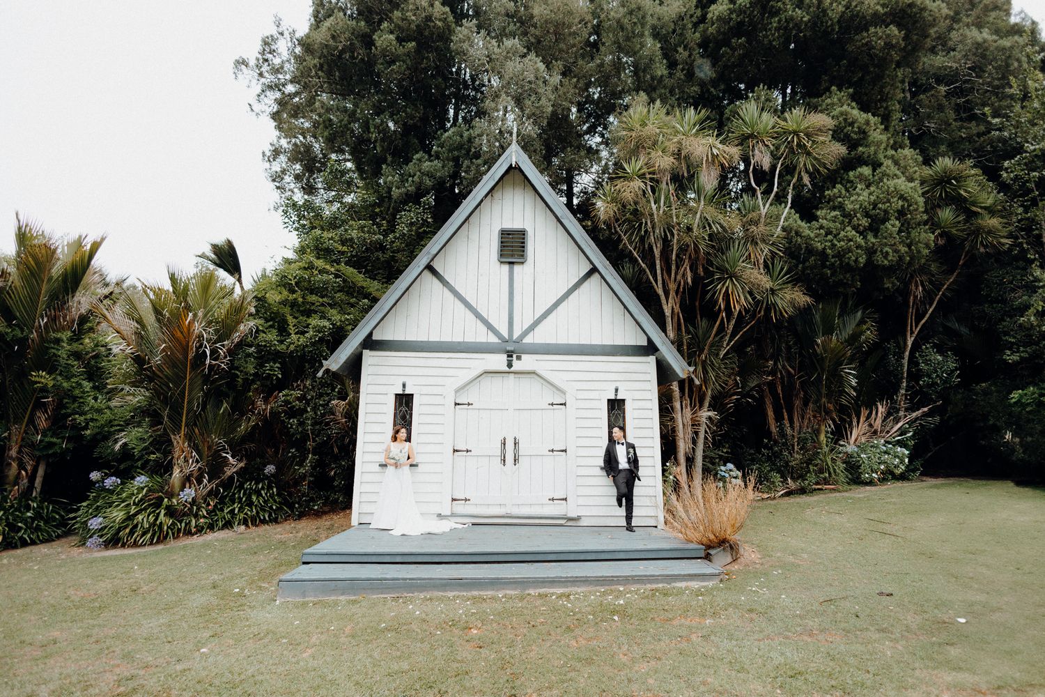 A small white chapel with Gothic architecture with the bride and groom captured by Apertured Media Auckland Wedding Photographer.