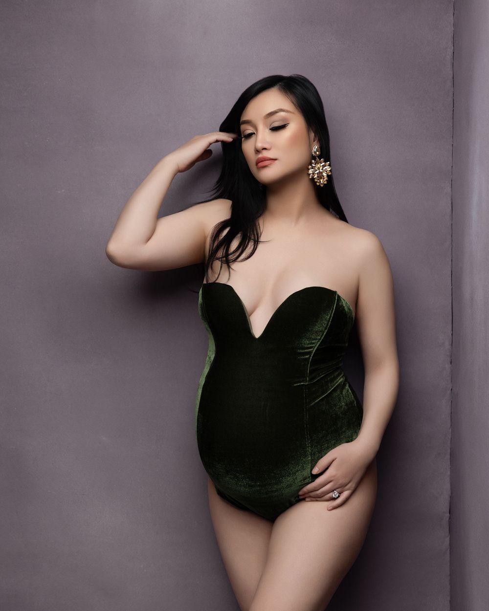 A glamour photo featuring a model in an elegant dark green velvet bodysuit against a gray backdrop.