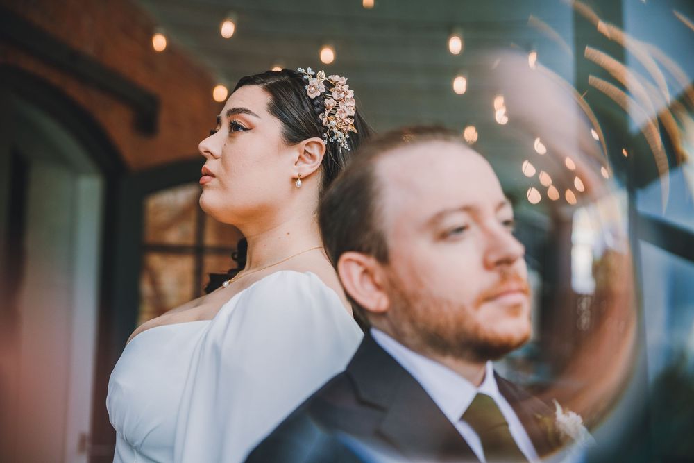 A couple poses back to back at their wedding, with the bride wearing a white dress and floral headpiece in an elegant venue.