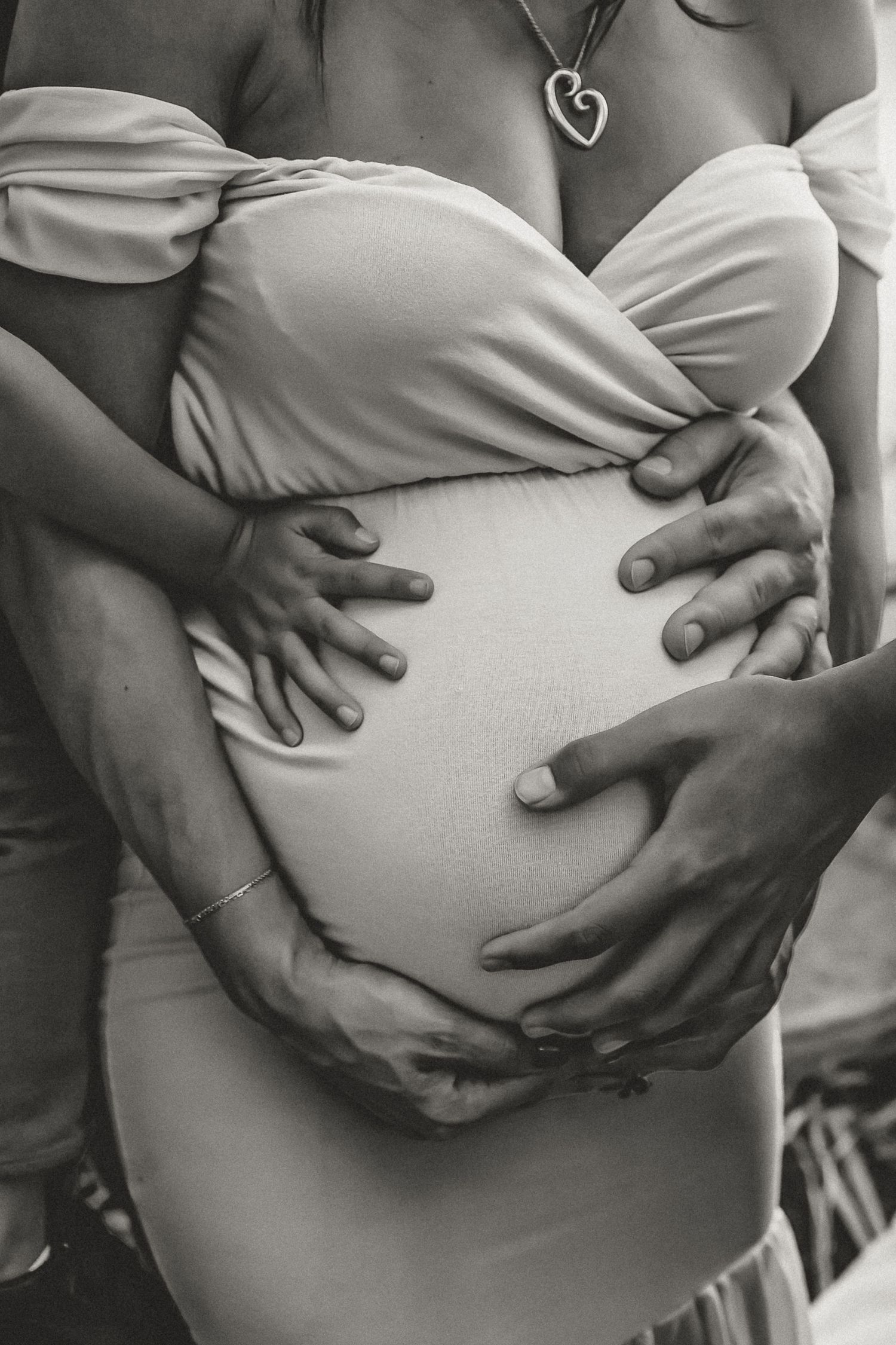 Black and white close-up of hands tenderly cradling pregnant belly wearing white top.