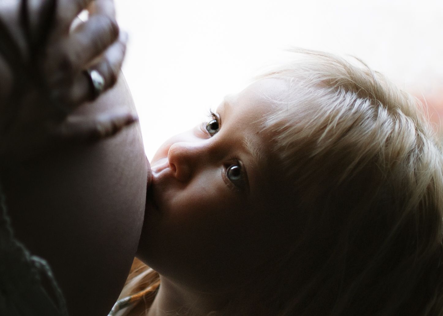 Little girl kissing her mother's pregnant belly