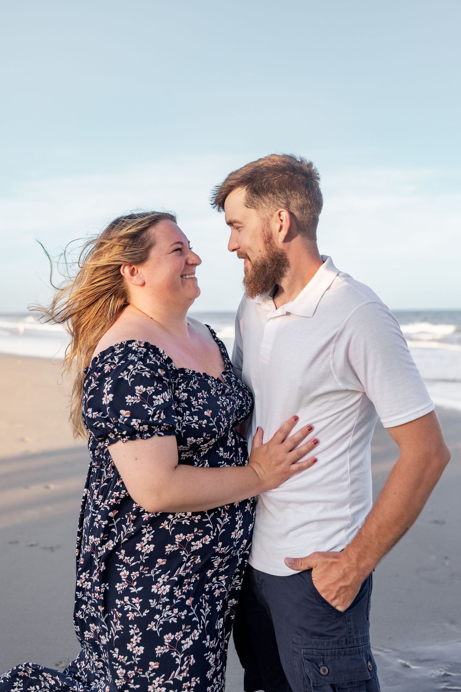A romantic couple laughing together during a seaside photoshoot at the beach with waves in the background.