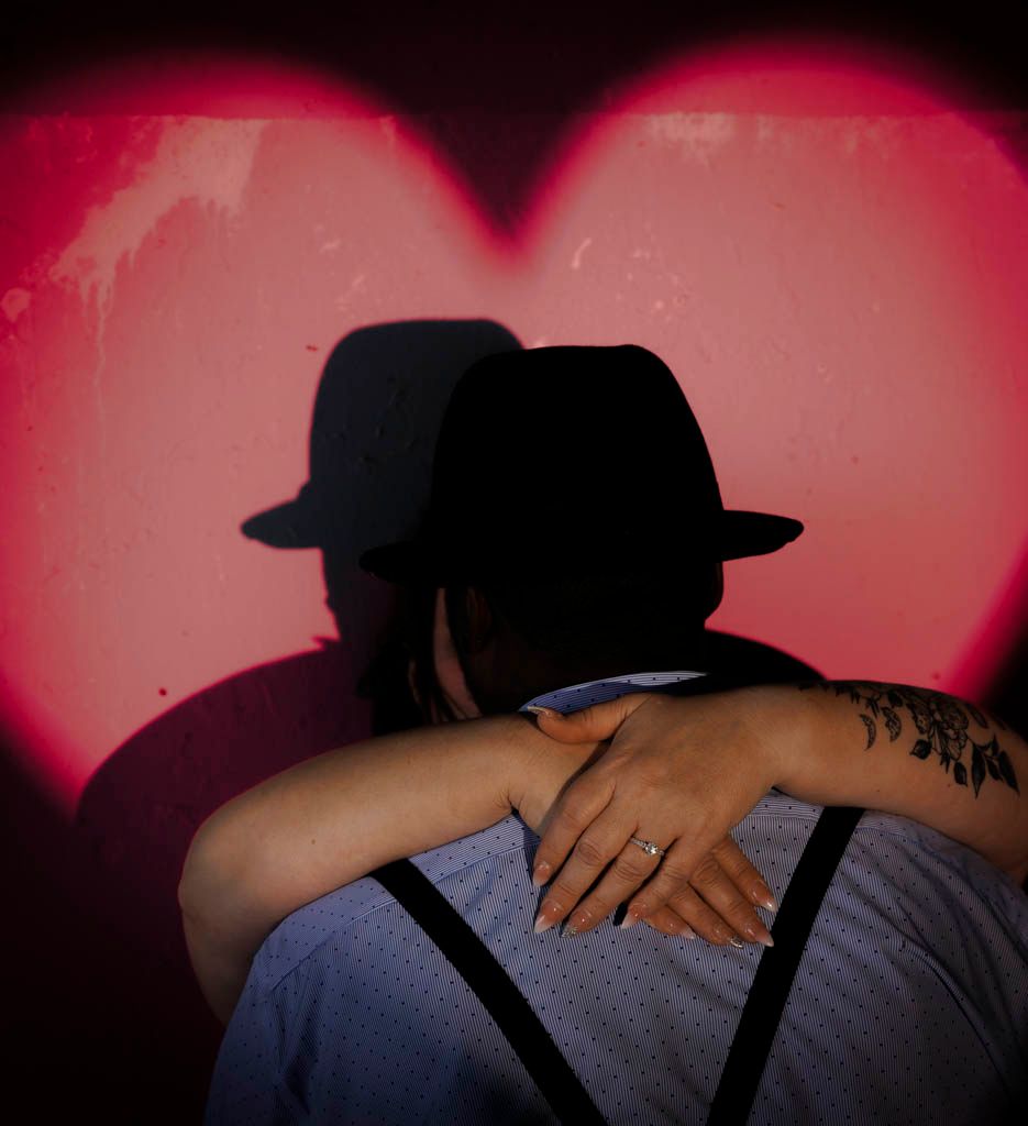Silhouette of embracing couple against red heart backdrop.