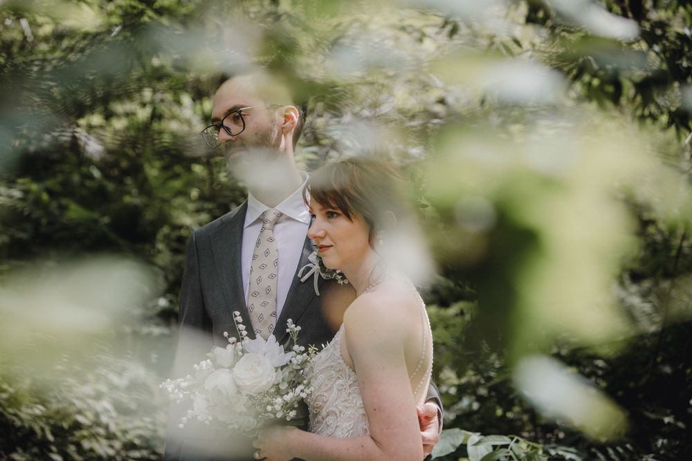 A couple shares an intimate moment in a sun-dappled forest setting during their wedding photoshoot.