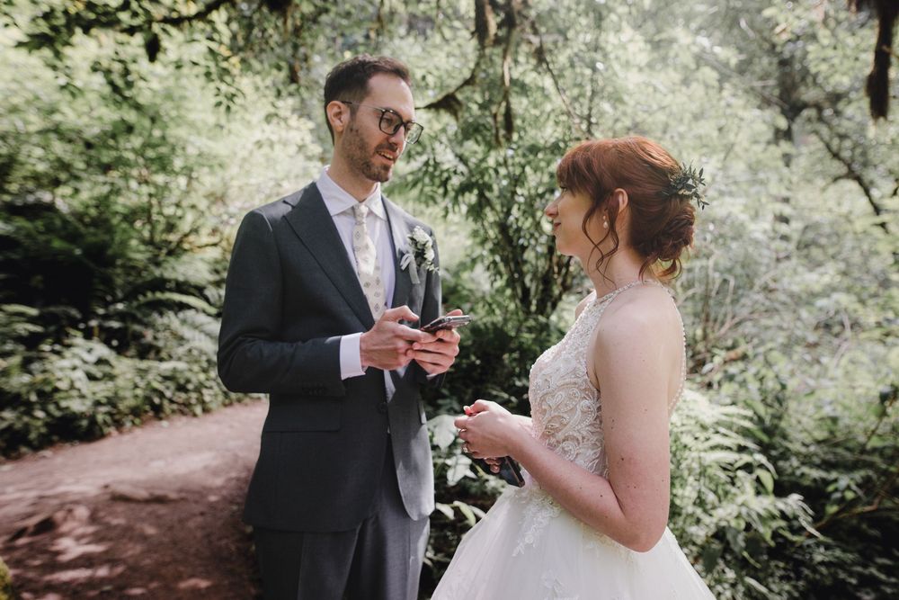 A couple shares a tender moment in a lush forest setting wearing formal wedding attire.
