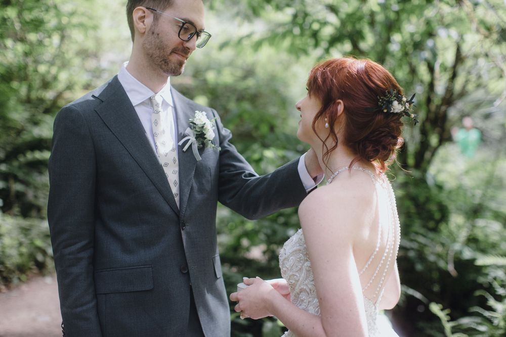 Wedding couple stands close together surrounded by green foliage in a romantic outdoor setting.