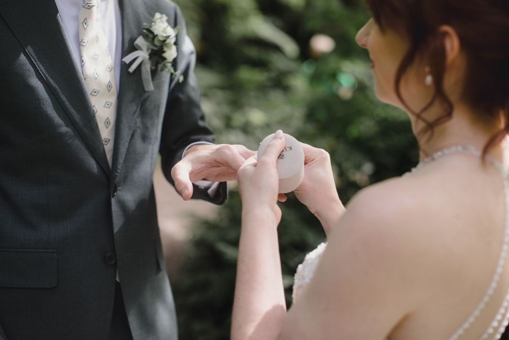 Close-up of a bride adjusting groom's boutonniere flower on his black suit jacket during wedding ceremony.
