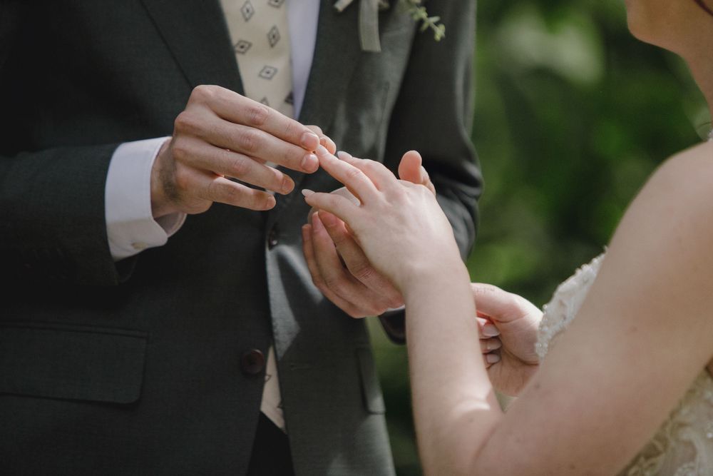 Close-up shot of hands exchanging wedding rings during an outdoor ceremony.