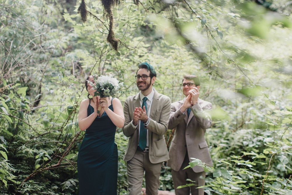 Wedding party members celebrate with champagne in a lush green forest setting.