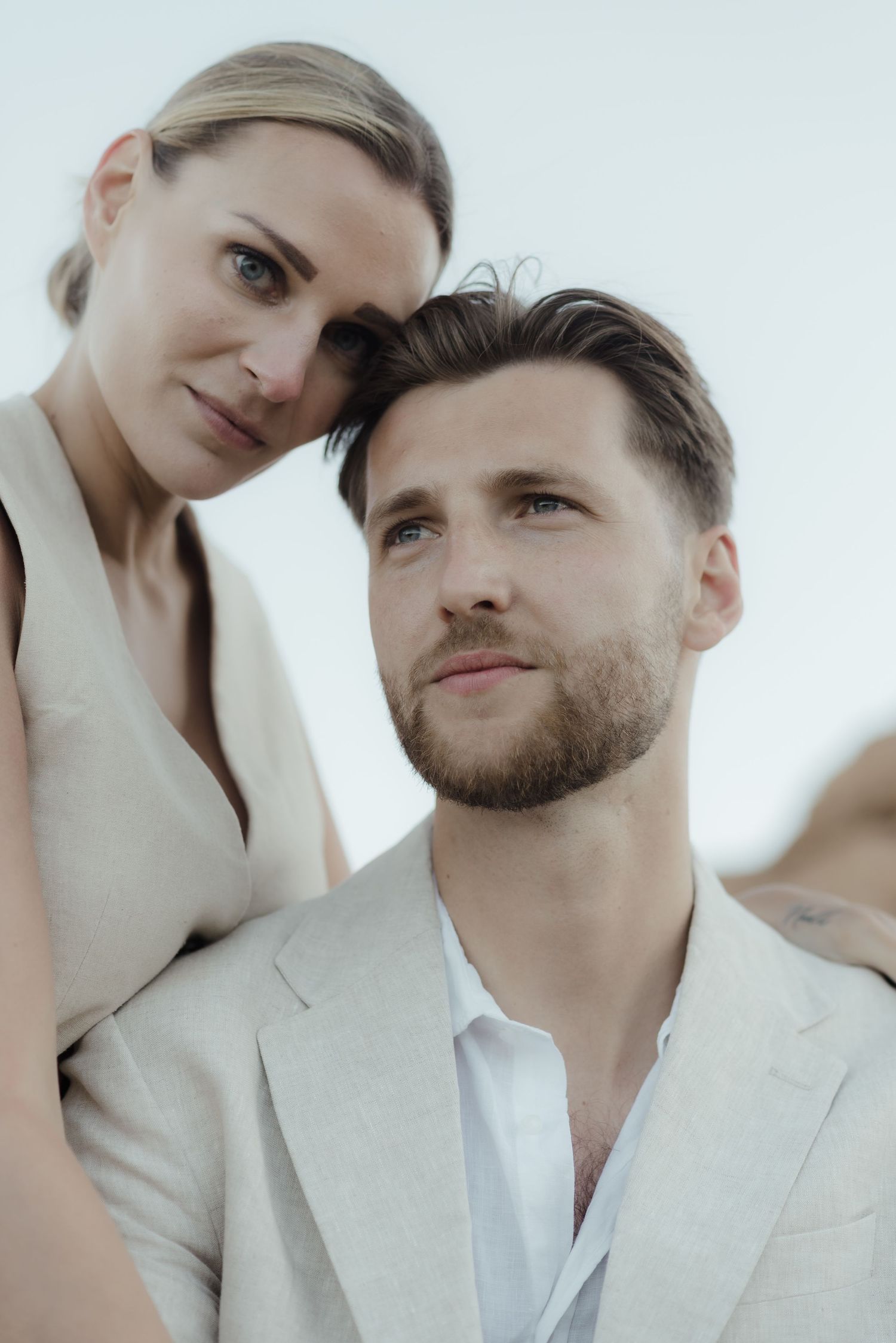 A stylish couple in white attire pose intimately against a light background for a fashion portrait.