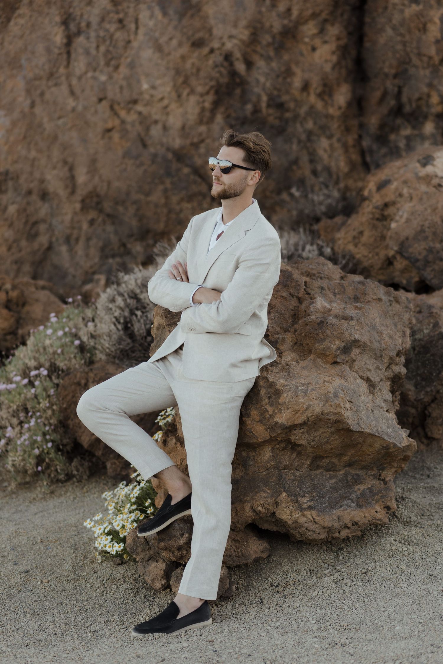 A person in a white suit and sunglasses poses against rocky terrain.