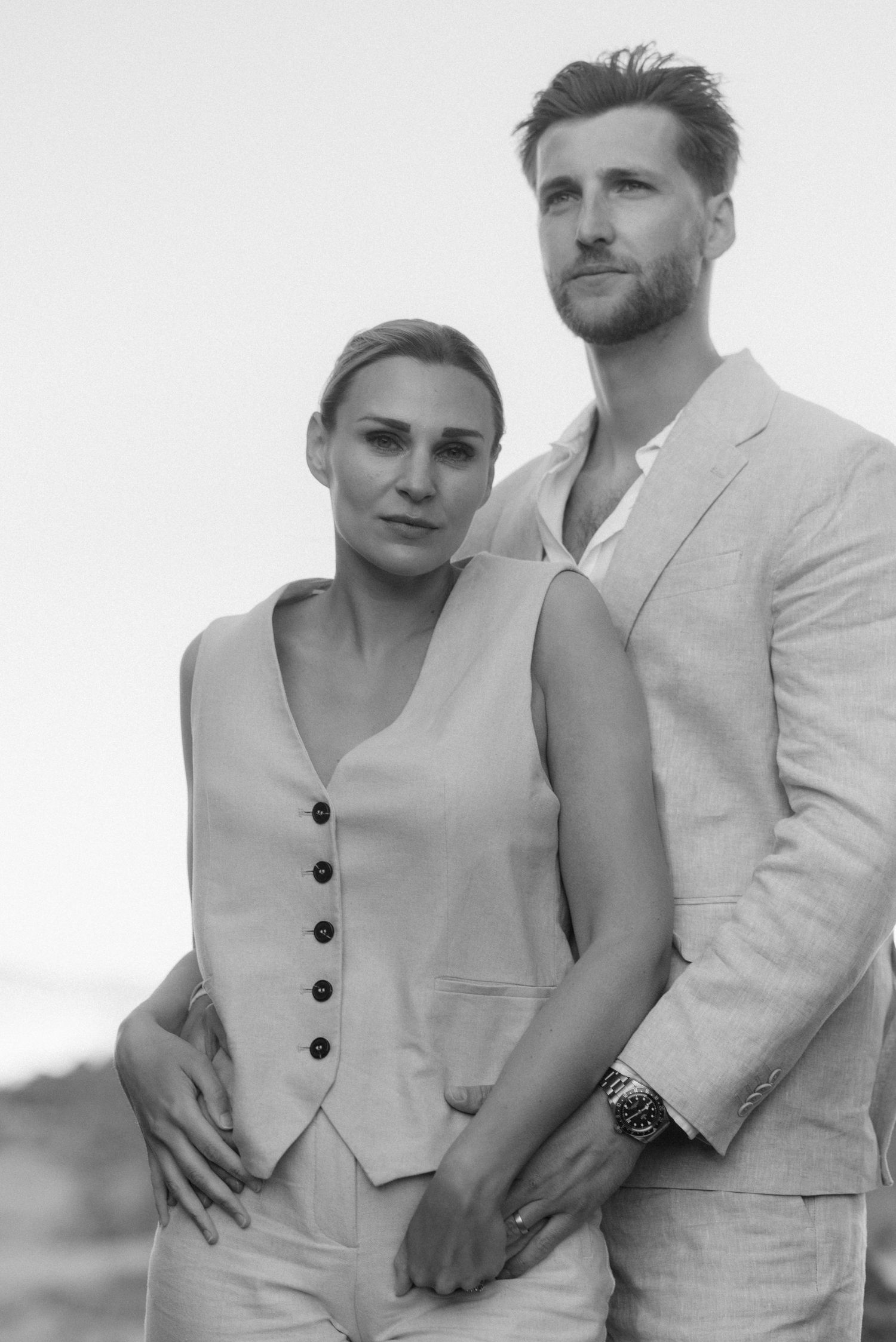 A couple in light colored formal wear poses together for a black and white portrait.