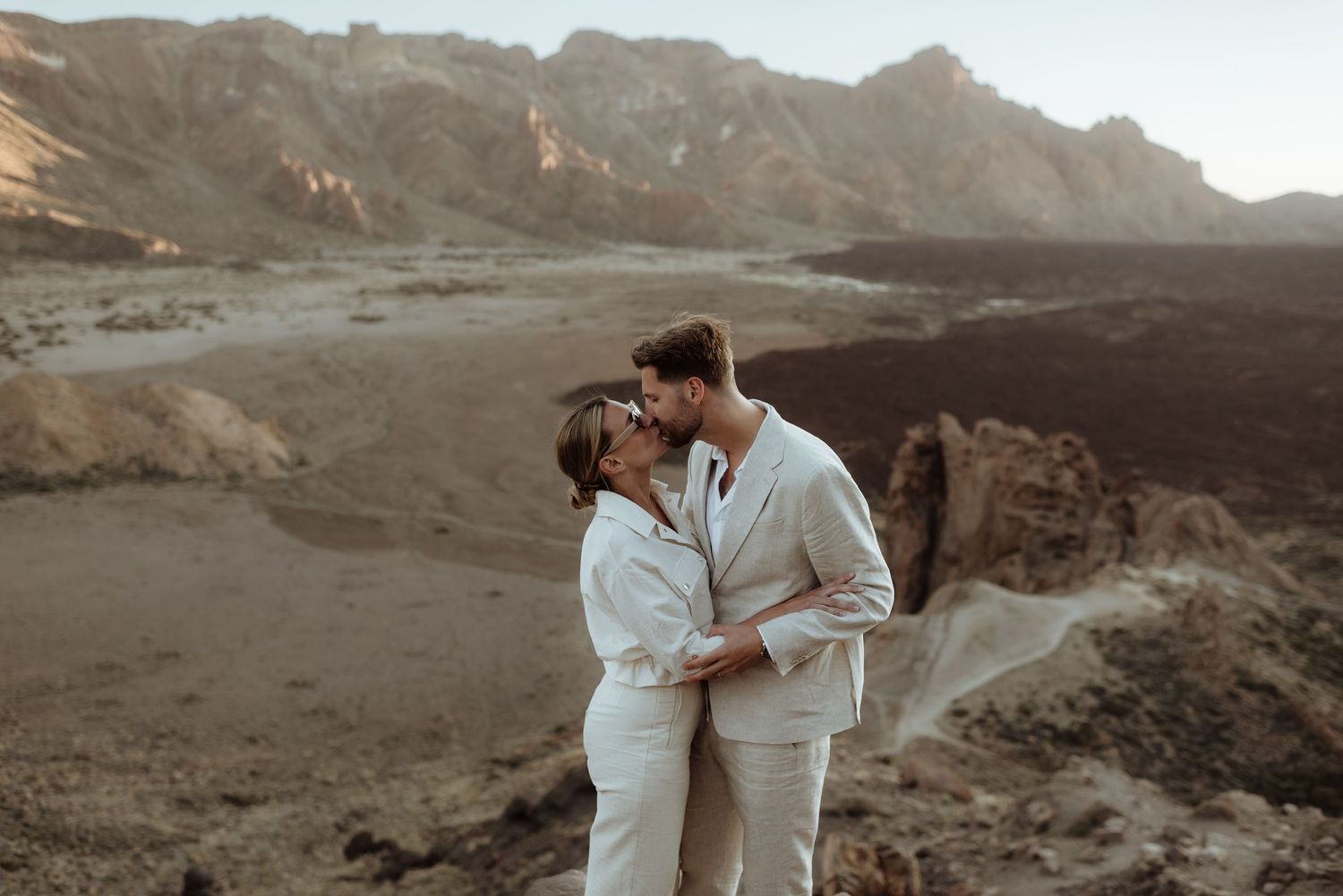 A romantic couple in white embracing among dramatic mountain scenery at sunset.