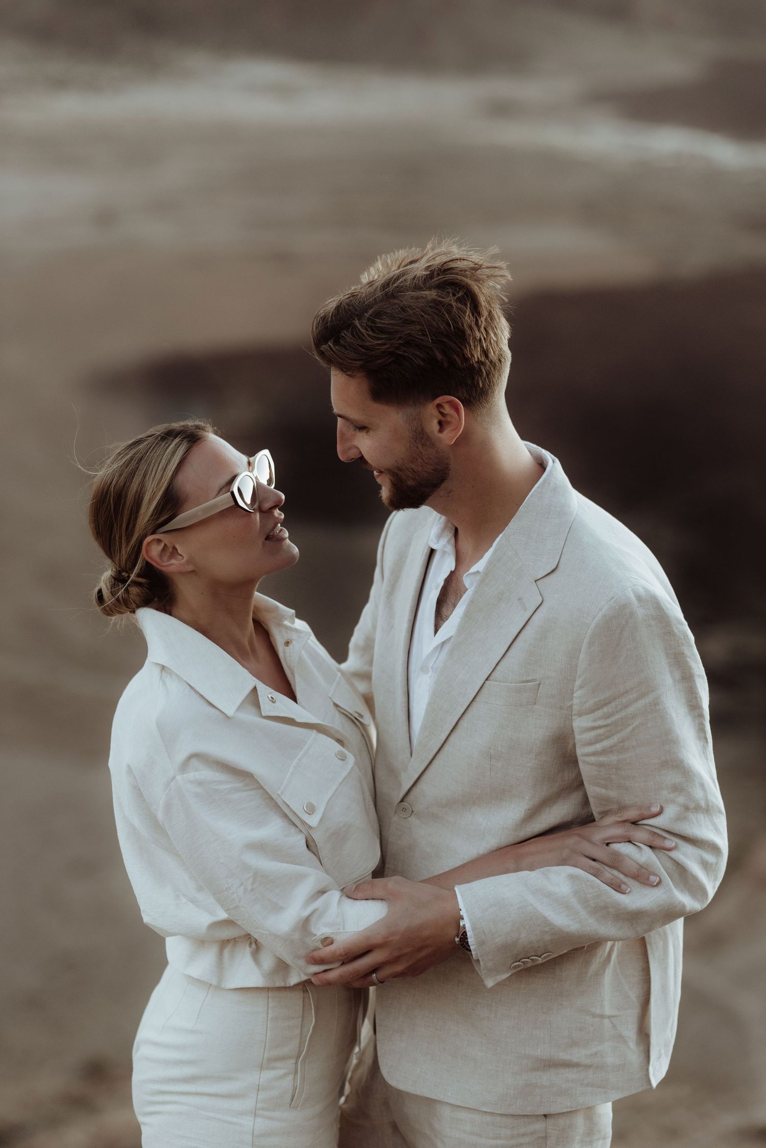 A tender moment captured between two people in matching white outfits against a desert backdrop.