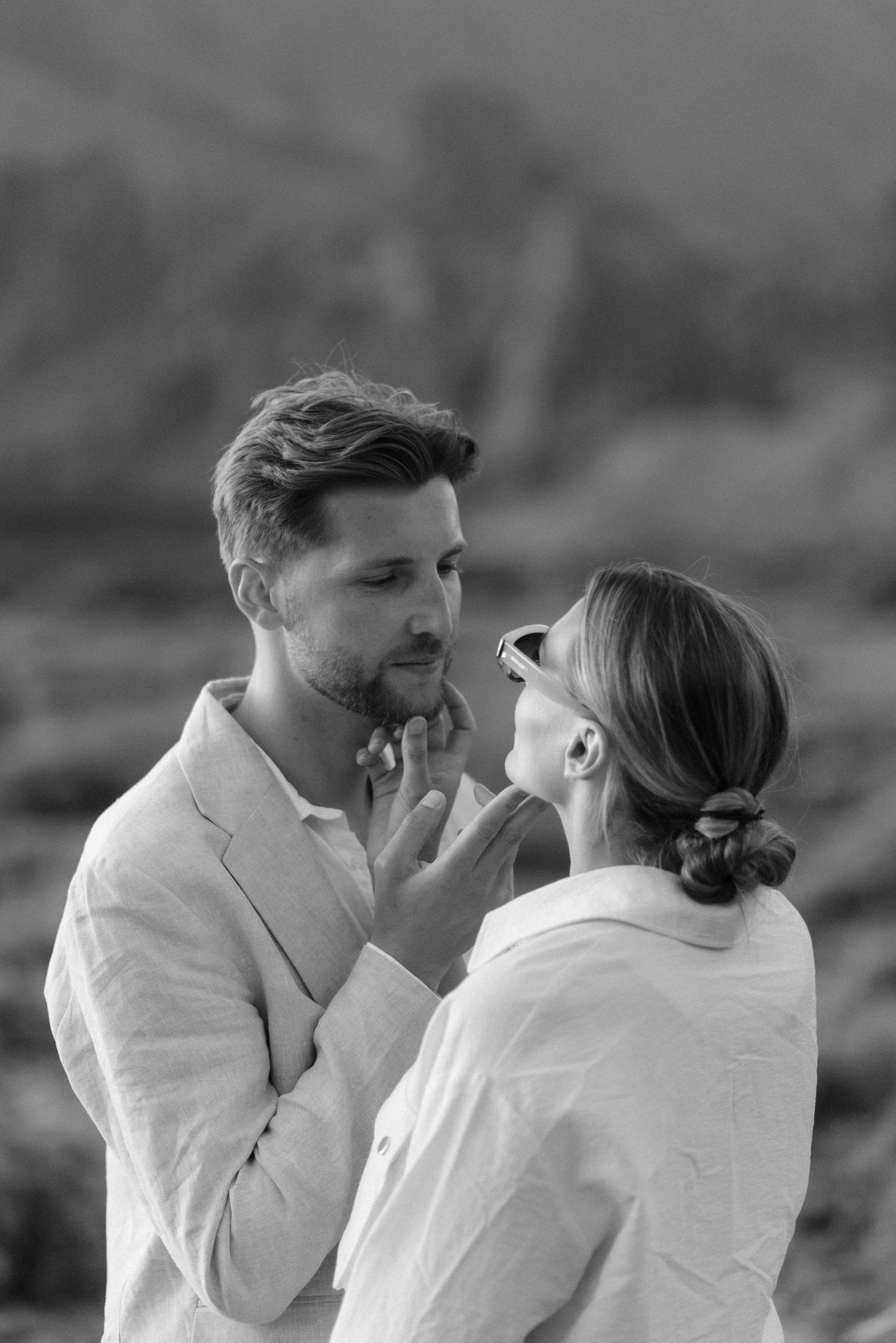 Close-up black and white photo of a couple sharing an intimate moment against a mountain backdrop.